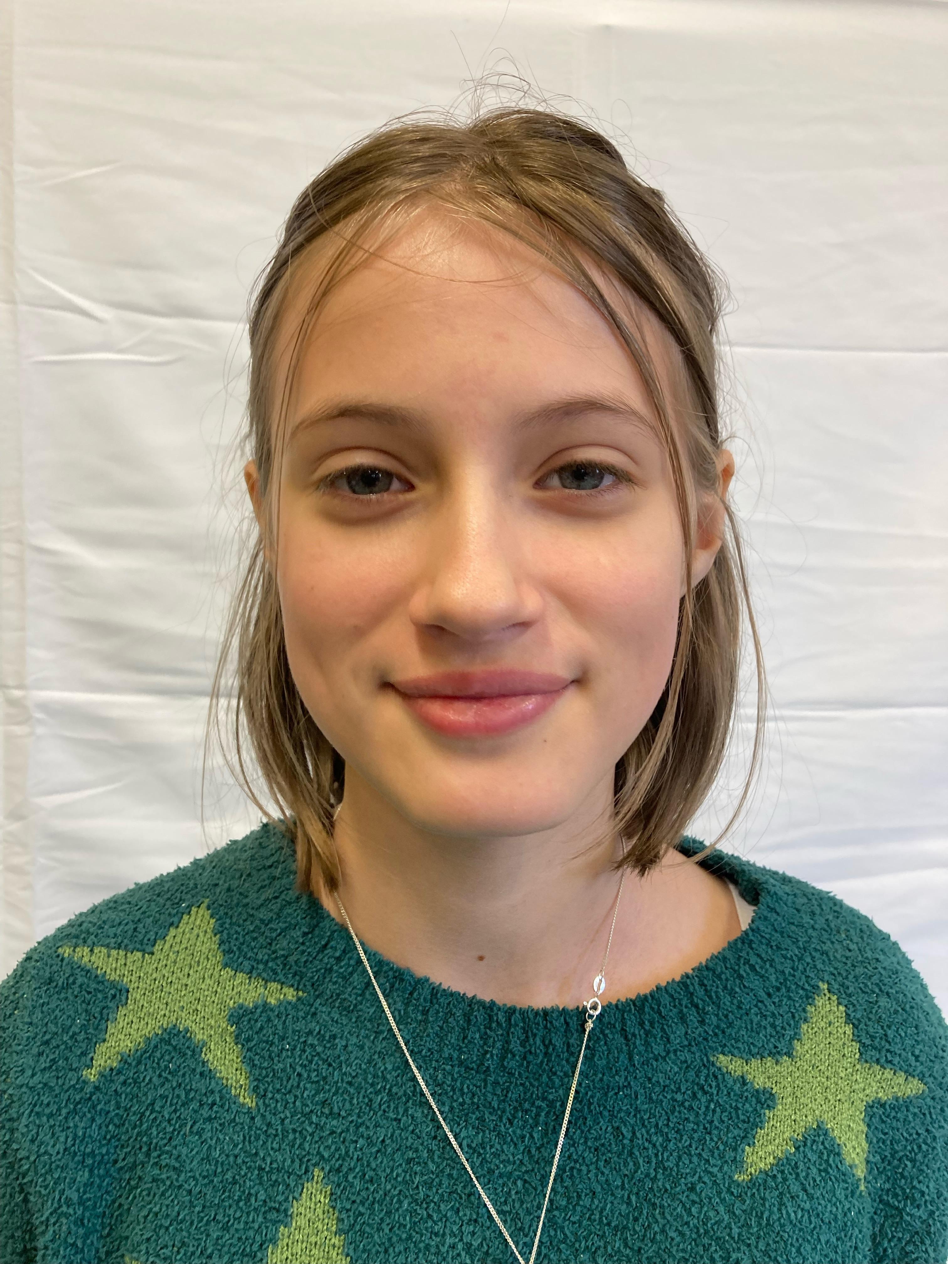 A girl with blonde hair and a green starred jumper poses for a profile picture.