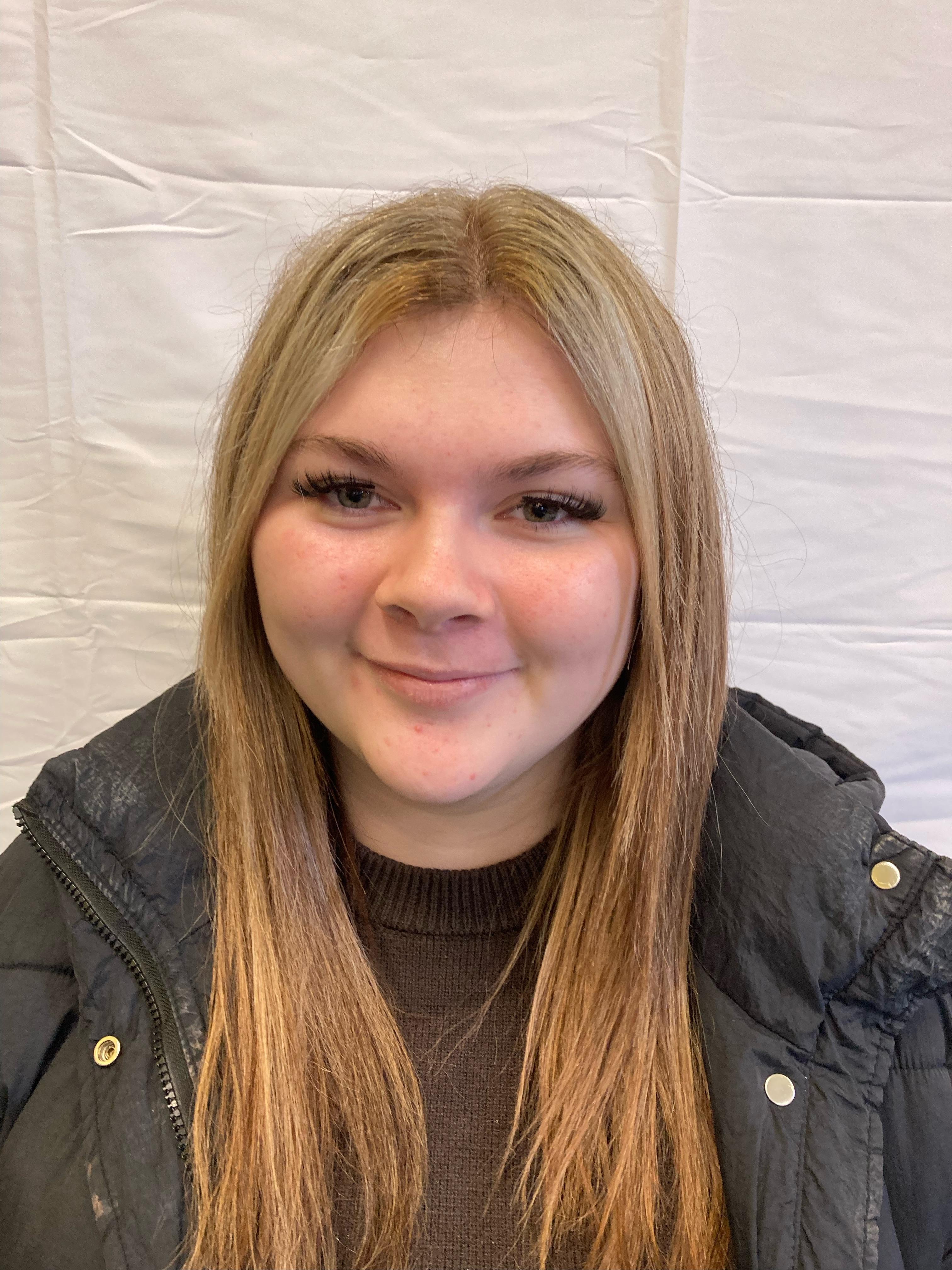 A girl with blonde hair wearing a black jacket poses for a profile picture.