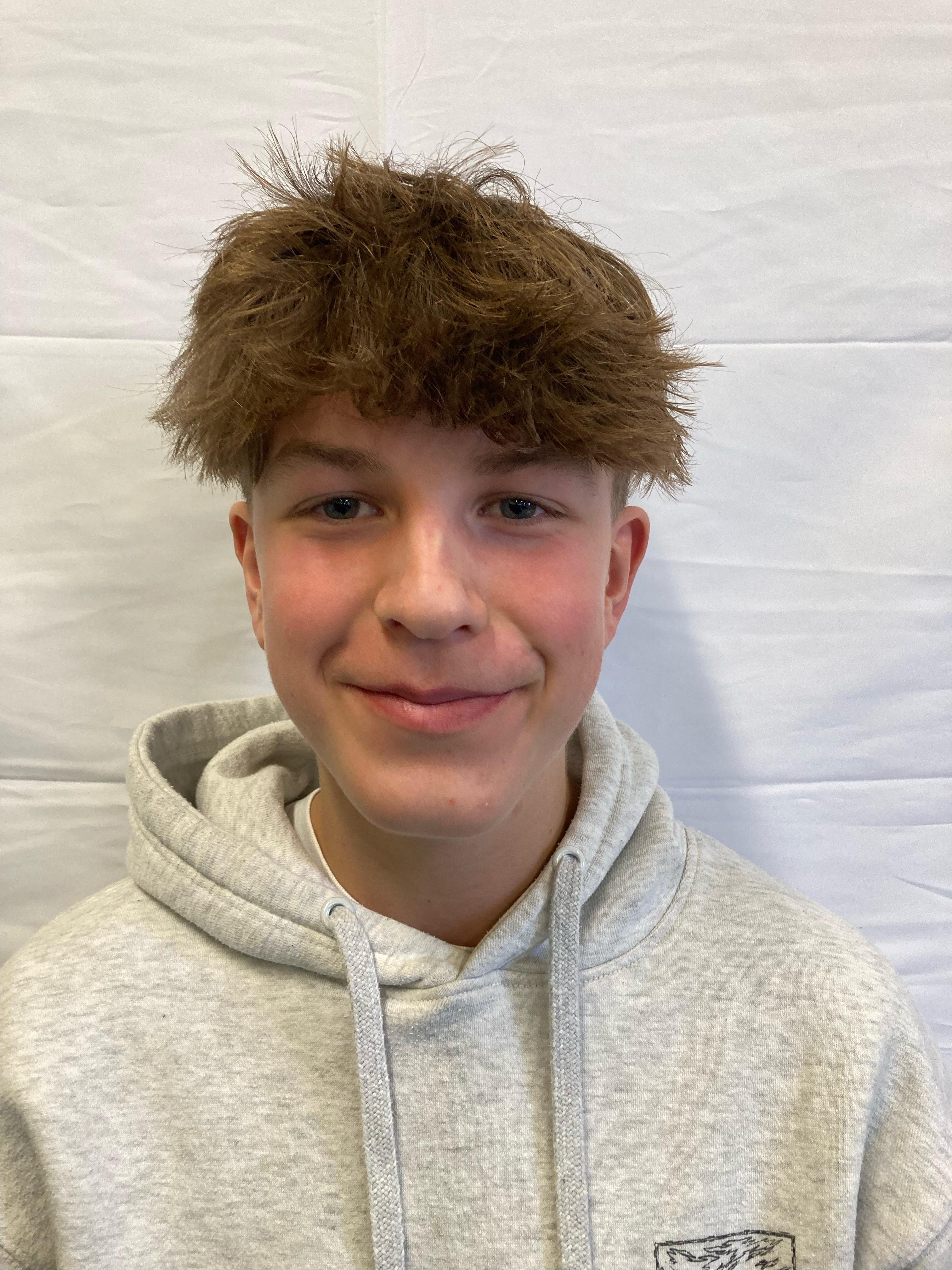 A boy with brunette hair wearing a grey hoodie poses for a profile picture.
