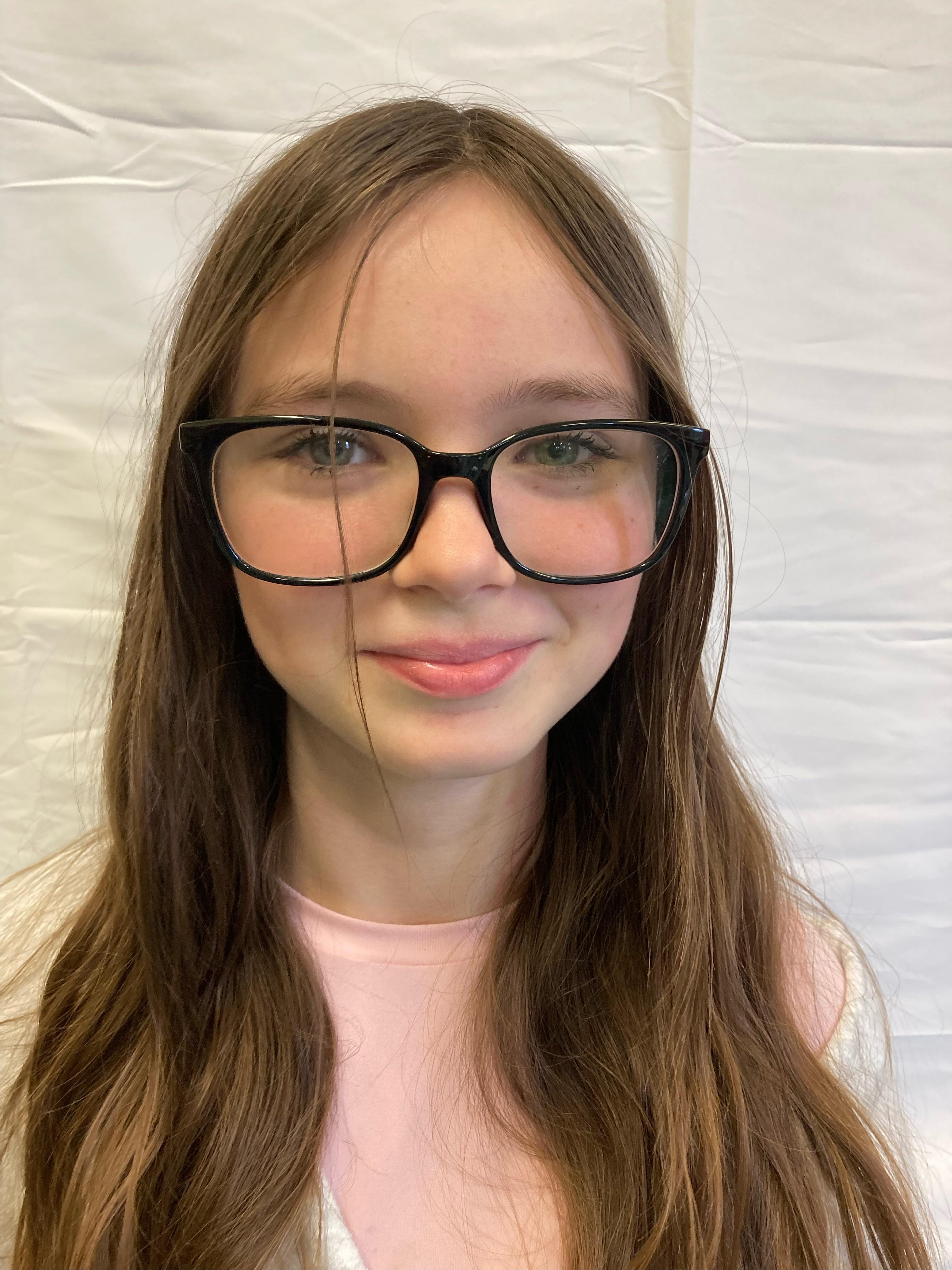 A girl with brunette hair and glasses poses for a profile picture.