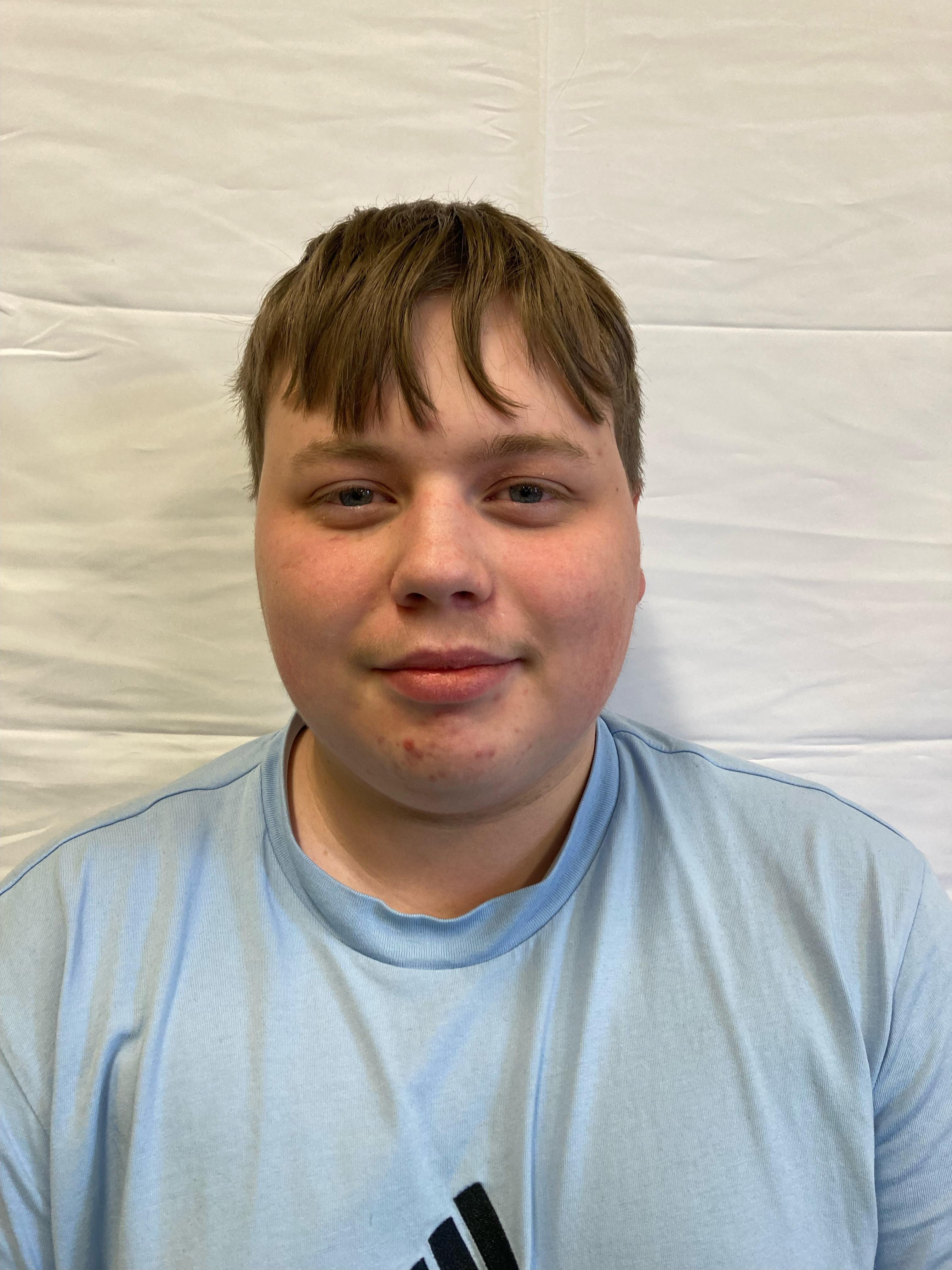 A boy with brunette hair wearing a blue t-shirt poses for a profile picture.