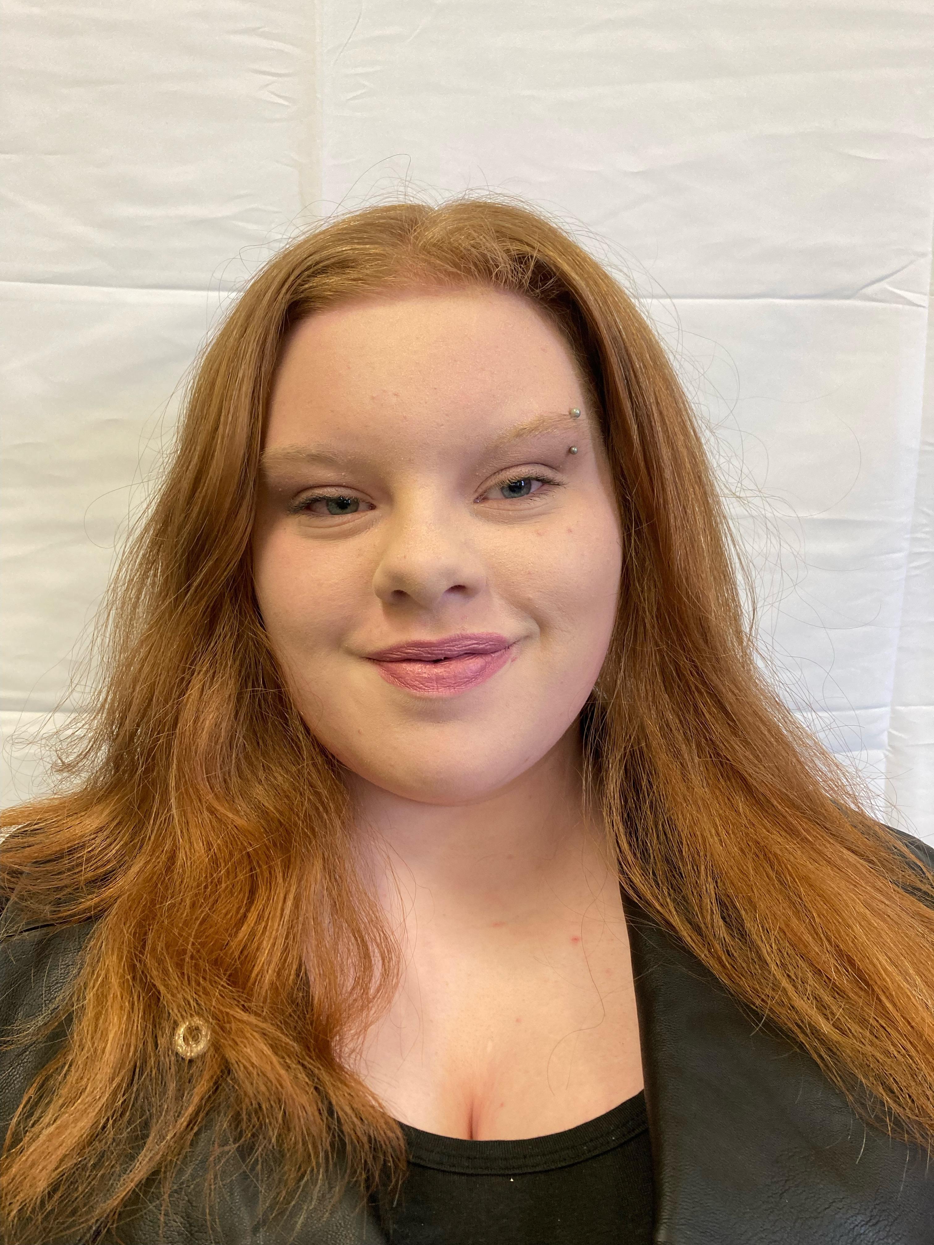 A girl with auburn hair and a black t-shirt and hoodie poses for a profile picture.