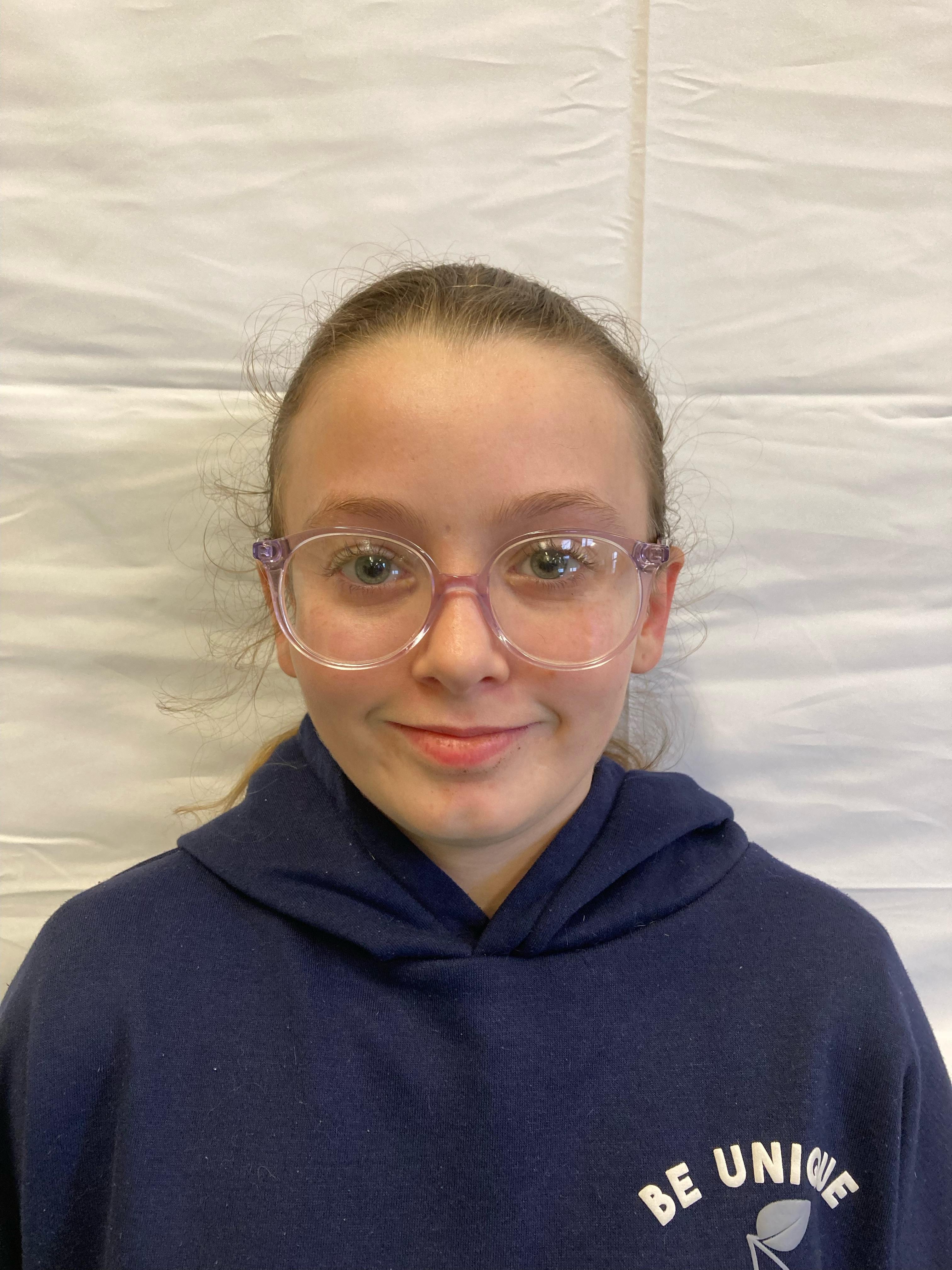 A girl with tied-up brunette hair and glasses poses for a profile picture.