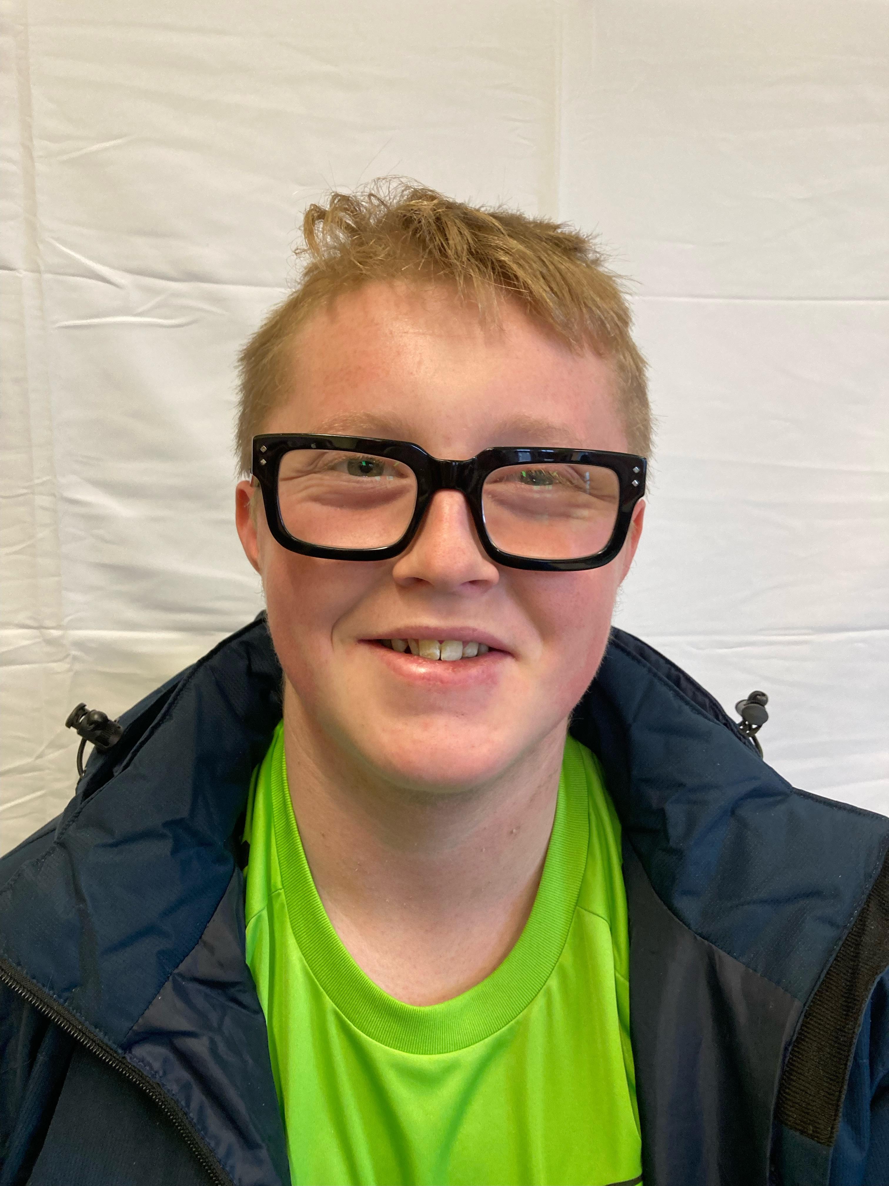 A boy with blonde hair and glasses wearing a green t-shirt poses for a profile picture.