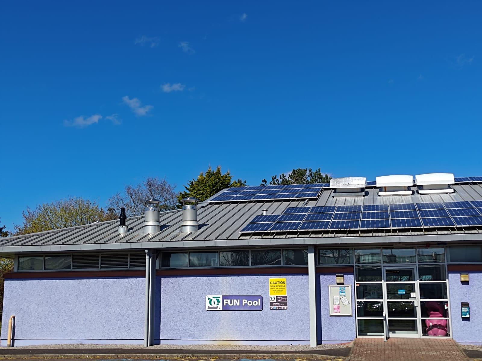 FUN Pool building with solar panels on the roof and glass entrance doors, under a blue sky.