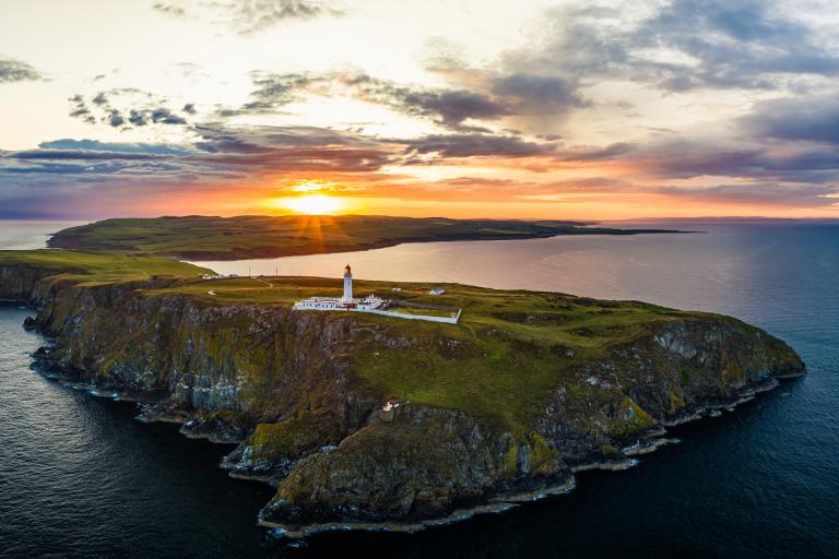 The lighthouse at Mull of Galloway is pictured against a setting sun and calm seascape. 