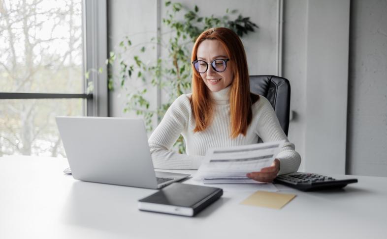 A person with glasses is at a desk, engaged with their laptop, surrounded by a neat and professional workspace
