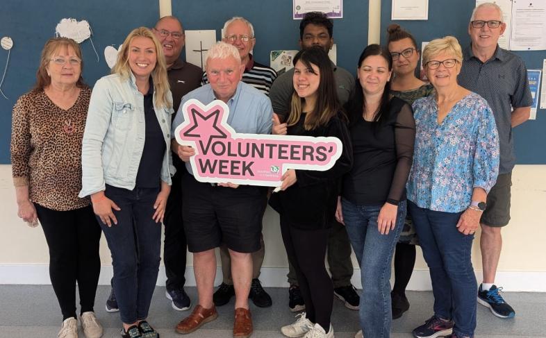 Volunteer adult support tutors hold up a Volunteers' Week sign.