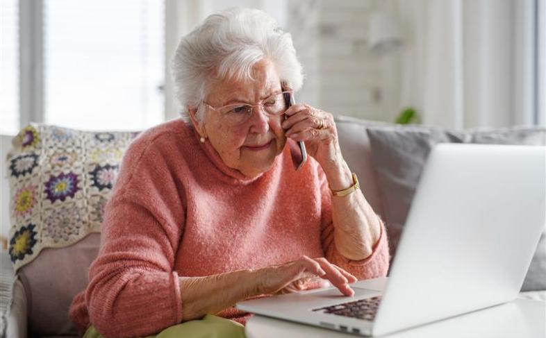 Senior citizen using a laptop and receiving a reassuring phone call 