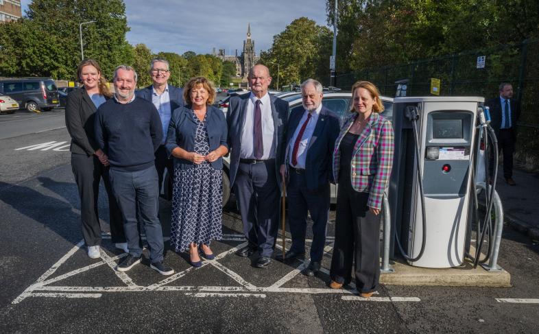 Scottish Cabinet Secretary for Transport, Fiona Hyslop MSP, and Dumfries and Galloway Council's Chair of Economy and Infrastructure Committee, Cllr. Andy Ferguson are joined by five other officials from across the South of Scotland in a photograph with a public EV charger in a carpark in Edinburgh. 