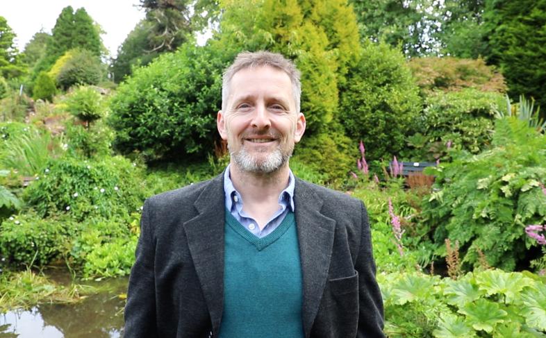 Cllr. Stephen Thompson smiles at the camera, pictured against the Crichton gardens on a bright day.