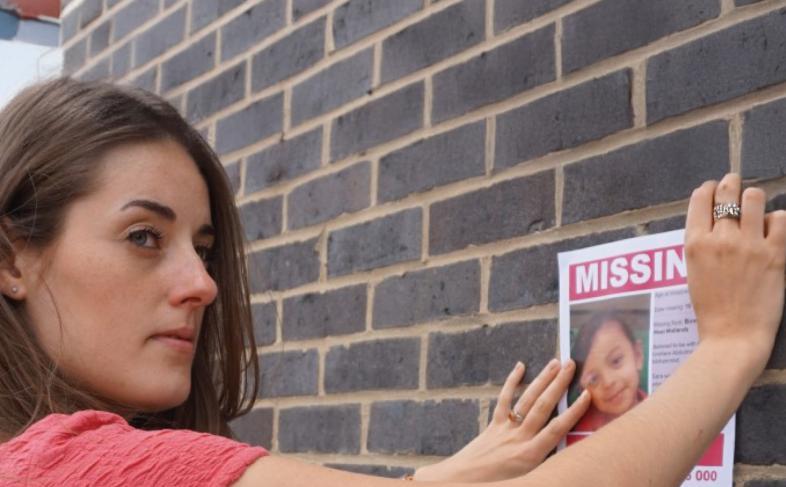 A person pastes a missing poster to a brick wall