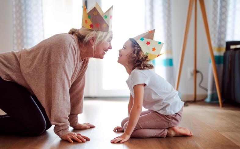 A grandmother and grand-daughter play together wearing paper crowns. 