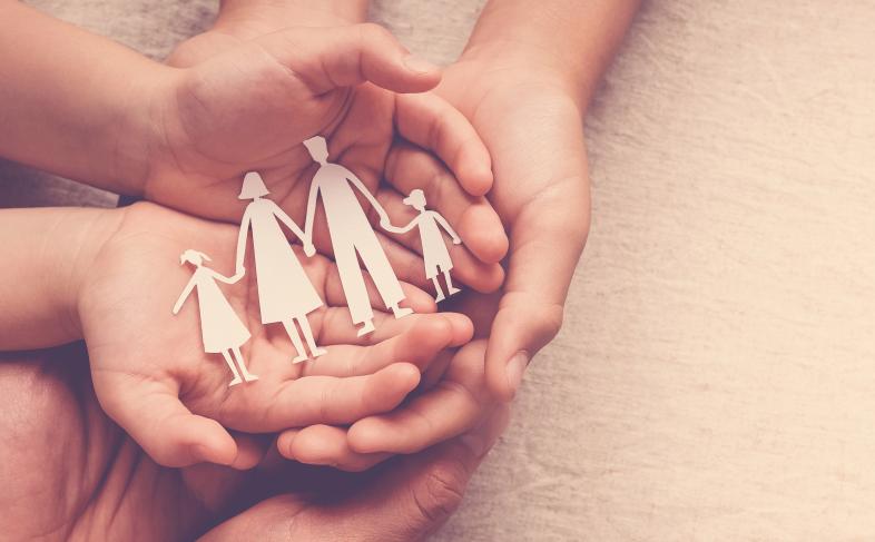 Hands holding paper family silhouettes of adults and children, symbolising care
