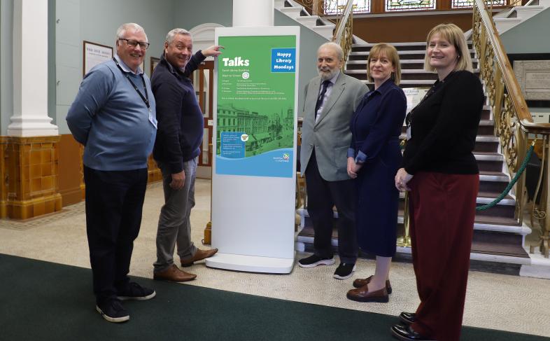 New digital display promoting library talks at Ewart Library, with five people standing alongside.