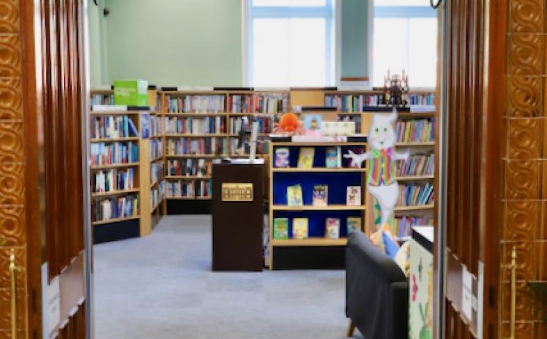 View through a carved wooden doorway into Ewart Library, with bookshelves and displays.
