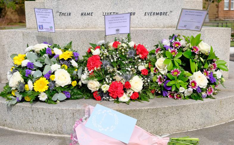 3 flower wreaths in a row beside a war memorial