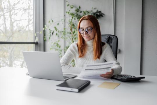 A person with glasses is at a desk, engaged with their laptop, surrounded by a neat and professional workspace