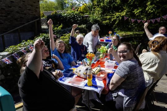 Service users at Newton Stewart ARC sit around a picnic table decorated with a Union flag for VE Day. 