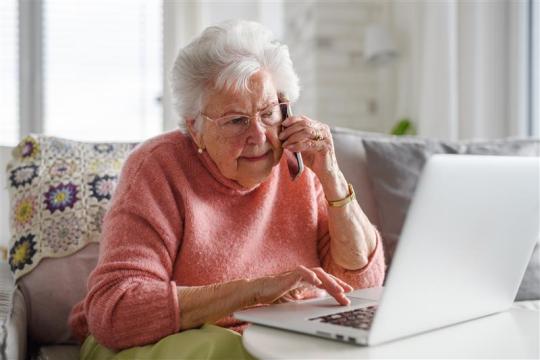 Senior citizen using a laptop and receiving a reassuring phone call 