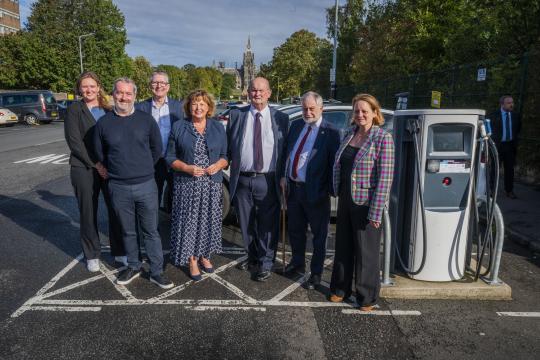 Scottish Cabinet Secretary for Transport, Fiona Hyslop MSP, and Dumfries and Galloway Council's Chair of Economy and Infrastructure Committee, Cllr. Andy Ferguson are joined by five other officials from across the South of Scotland in a photograph with a public EV charger in a carpark in Edinburgh. 