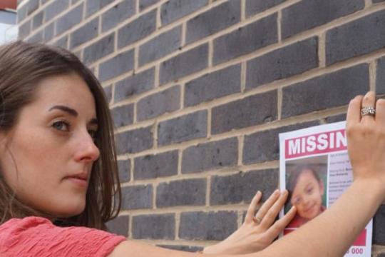 A person pastes a missing poster to a brick wall