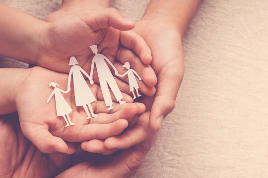 Hands holding paper family silhouettes of adults and children, symbolising care