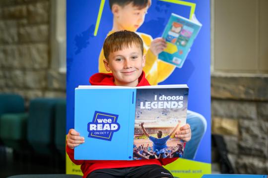 Child holding an open Wee Read book with “I choose legends” on the cover.