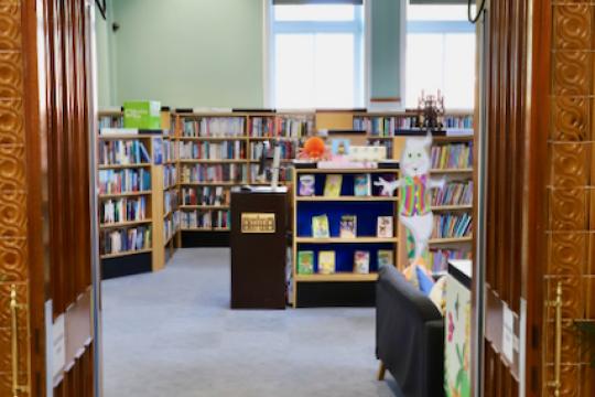 View through a carved wooden doorway into Ewart Library, with bookshelves and displays.
