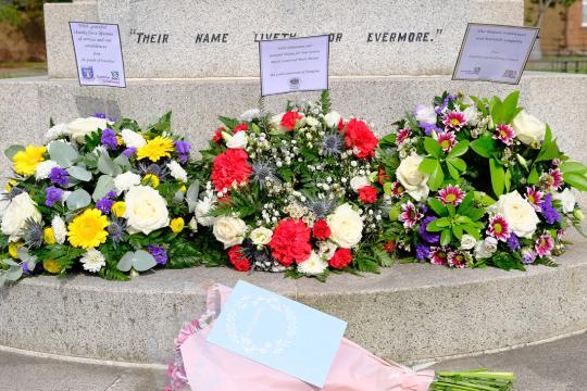 3 flower wreaths in a row beside a war memorial